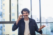 Усміхнений чоловік розмовляє по смартфону в міській квартирі — стокове фото