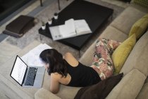 Женщина в пижаме работает за ноутбуком на диване в гостиной — стоковое фото