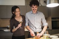 Счастливая пара готовит ужин и пьет белое вино на кухне квартиры — стоковое фото