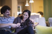 Verspieltes Paar kämpft um die Fernbedienung, schaut fern und trinkt Weißwein auf dem Sofa — Stockfoto