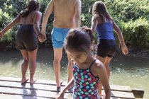 Family playing, jumping off dock into sunny river — Stock Photo