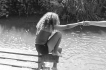 Девушка, сидящая на краю солнечного причала у реки — стоковое фото