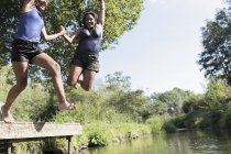 Playful mother and daughter jumping into sunny river — Stock Photo