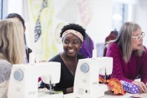 Diseñadora de moda femenina feliz trabajando, hablando con su colega en la máquina de coser - foto de stock