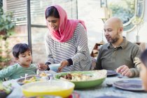 Mother in hijab serving dinner to family at table — Stock Photo