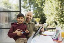 Retrato feliz padre e hijo para colorear y usar tableta digital en la mesa - foto de stock