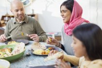 Счастливая женщина в хиджабе ужинает с семьей за столом — стоковое фото