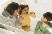 Madre e hijos cepillándose los dientes en el baño - foto de stock