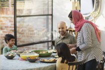 Mother in hijab serving dinner to family at dining table — Stock Photo