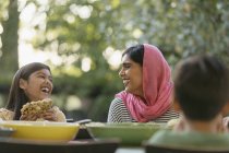 Madre en hijab e hija riendo en la mesa de la cena - foto de stock