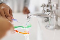 Close up family rinsing toothbrushes in bathroom sink — Stock Photo