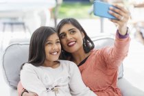 Feliz madre e hija tomando selfie con teléfono inteligente en sillón - foto de stock