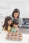 Madre e hijos horneando magdalenas de chocolate en la cocina - foto de stock