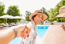 Счастливая жена, ведущая мужа за руку на солнечном курорте у бассейна — стоковое фото