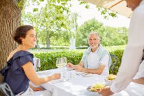 Camarero sirviendo comida a pareja madura cenando en la mesa del patio - foto de stock