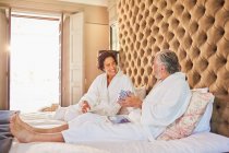 Mature couple in bathrobes on hotel bed — Stock Photo