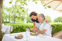 Mature couple dining, using smart phone at patio table — Stock Photo