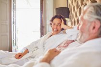 Счастливая, смеющаяся зрелая пара отдыхает на гостиничной кровати — стоковое фото