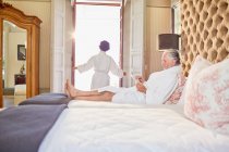 Mature couple in bathrobes relaxing in hotel bedroom — Stock Photo