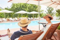 Couple relaxing on lounge chairs at resort poolside — Stock Photo