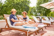 Mature couple relaxing on lounge chairs at sunny poolside — Stock Photo