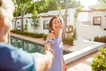 Happy, carefree mature couple holding hands at sunny resort poolside — Stock Photo