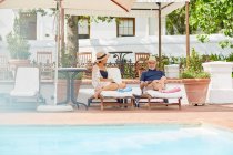 Mature couple relaxing on lounge chairs at resort poolside — Stock Photo