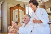 Happy mature couple in spa bathrobes drinking coffee in hotel room — Stock Photo