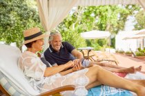 Mature couple relaxing, using smart phone on lounge chairs in resort cabana — Stock Photo