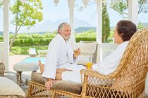 Pareja madura en albornoces relajantes, bebiendo mimosas en el gazebo del resort - foto de stock