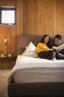 Livro de leitura de casal e usando tablet digital na cama — Fotografia de Stock