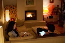 Casal usando tablet digital e telefone inteligente na sala de estar — Fotografia de Stock