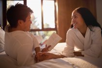 Pareja en albornoces leyendo libro en la cama - foto de stock