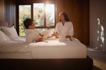 Couple in bathrobes relaxing on hotel bed — Stock Photo