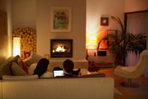 Couple using digital tablet on living room sofa facing fireplace — Stock Photo
