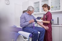 Infermiera donna che controlla la pressione sanguigna del paziente di sesso maschile anziano nella sala esami della clinica — Foto stock