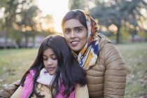 Портрет улыбающейся матери в хиджабе, сидящей в осеннем парке с дочерью — стоковое фото