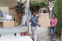 Couple moving out of house, carrying boxes to moving van — Stock Photo