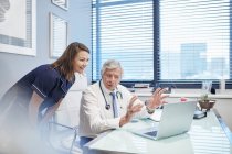 Arzt und Krankenschwester sprechen am Laptop in Arztpraxis — Stockfoto