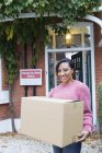 Retrato feliz, mujer segura de sí misma mudanza casa, llevando caja de cartón en la entrada - foto de stock