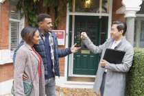 Real estate agent giving house keys to couple outside house for sale — Stock Photo