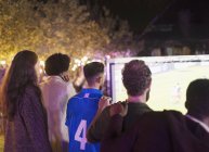 Друзі дивляться футбольний матч на проекційному екрані на задньому дворі — стокове фото