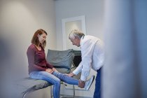 Male doctor examining woman leg in clinic examination room — Stock Photo