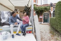 Couple talking and drinking tea, taking a break at back of moving van outside new house — Stock Photo