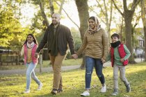 Familia musulmana cogida de la mano, caminando en el parque de otoño - foto de stock