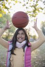 Portrait cute girl balancing basketball on head in autumn park — Stock Photo