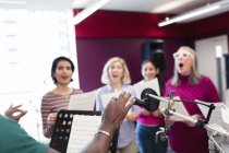 Male conductor leading women choir with sheet music singing in music recording studio — Stock Photo