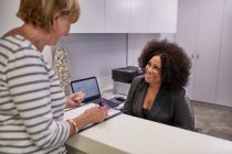 Mujer mayor registrándose con la recepcionista en la clínica - foto de stock