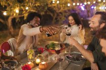 Amici versando e bevendo vino, godendo cena in giardino festa — Foto stock
