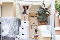 Retrato menina brincalhão pulando de trás caixas de papelão em van em movimento — Fotografia de Stock